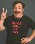 Smiling man with mustache wearing a black “All Of Life Is Art” t-shirt, flashing a peace sign.