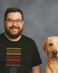 Smiling man with glasses and a beard wearing a black t-shirt that says ‘Round Earth Society’ in colorful text, standing next to a yellow Labrador Retriever dog