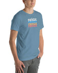 Angled front view of a man wearing a Milk Sandwich steel blue t-shirt with a colorful distressed relax text design repeated vertically in white, blue, orange, and pink.