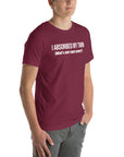 Man wearing maroon “I ABSORBED MY TWIN (What’s your super power?)” t-shirt, standing angled to the side with hands in pockets.