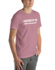 Man wearing orchid “I ABSORBED MY TWIN (What’s your super power?)” t-shirt, standing angled to the side with hands in pockets.