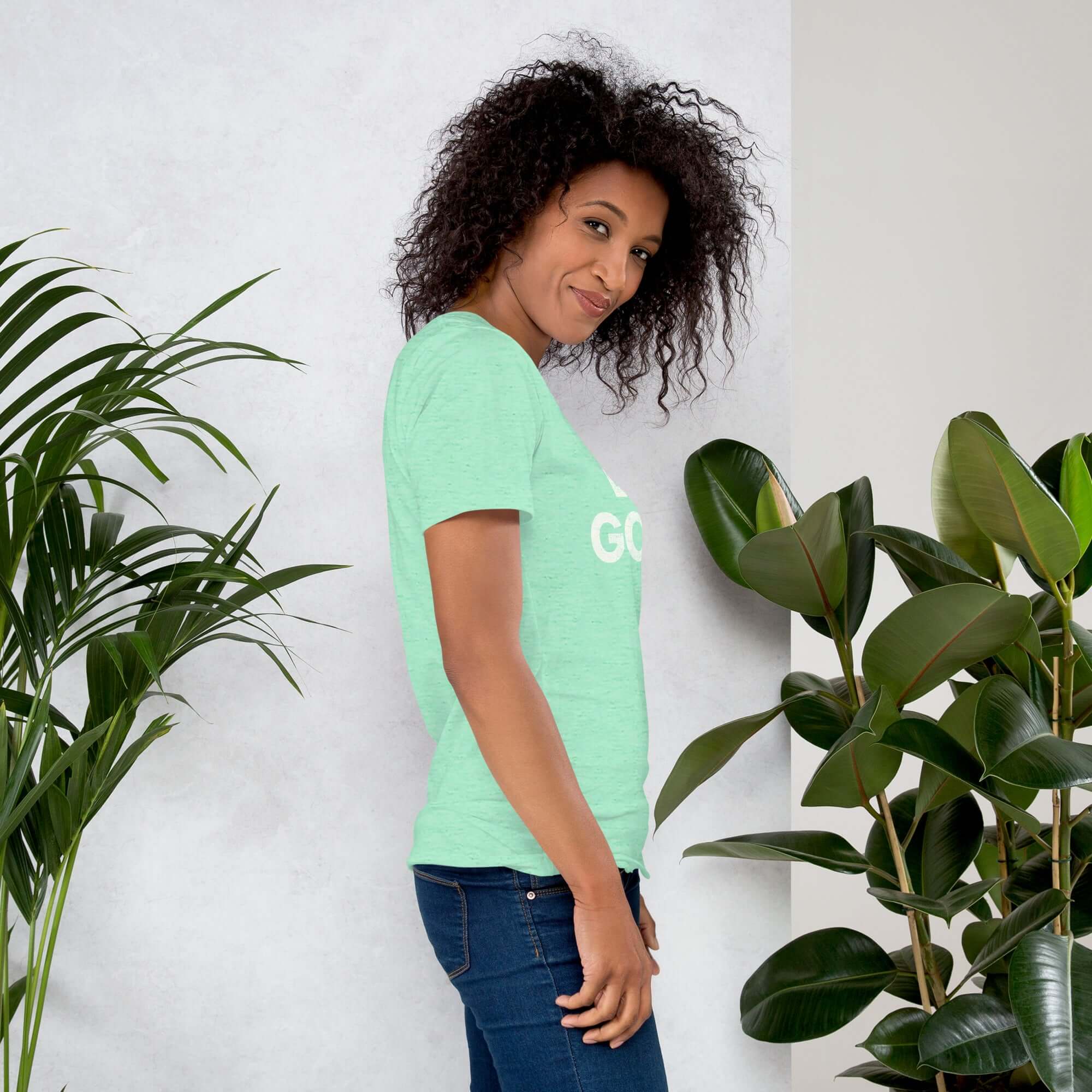 Side profile of smiling woman in heather mint Milk Sandwich T-shirt with DO GOOD text, standing near plants, casual inspirational graphic tee.