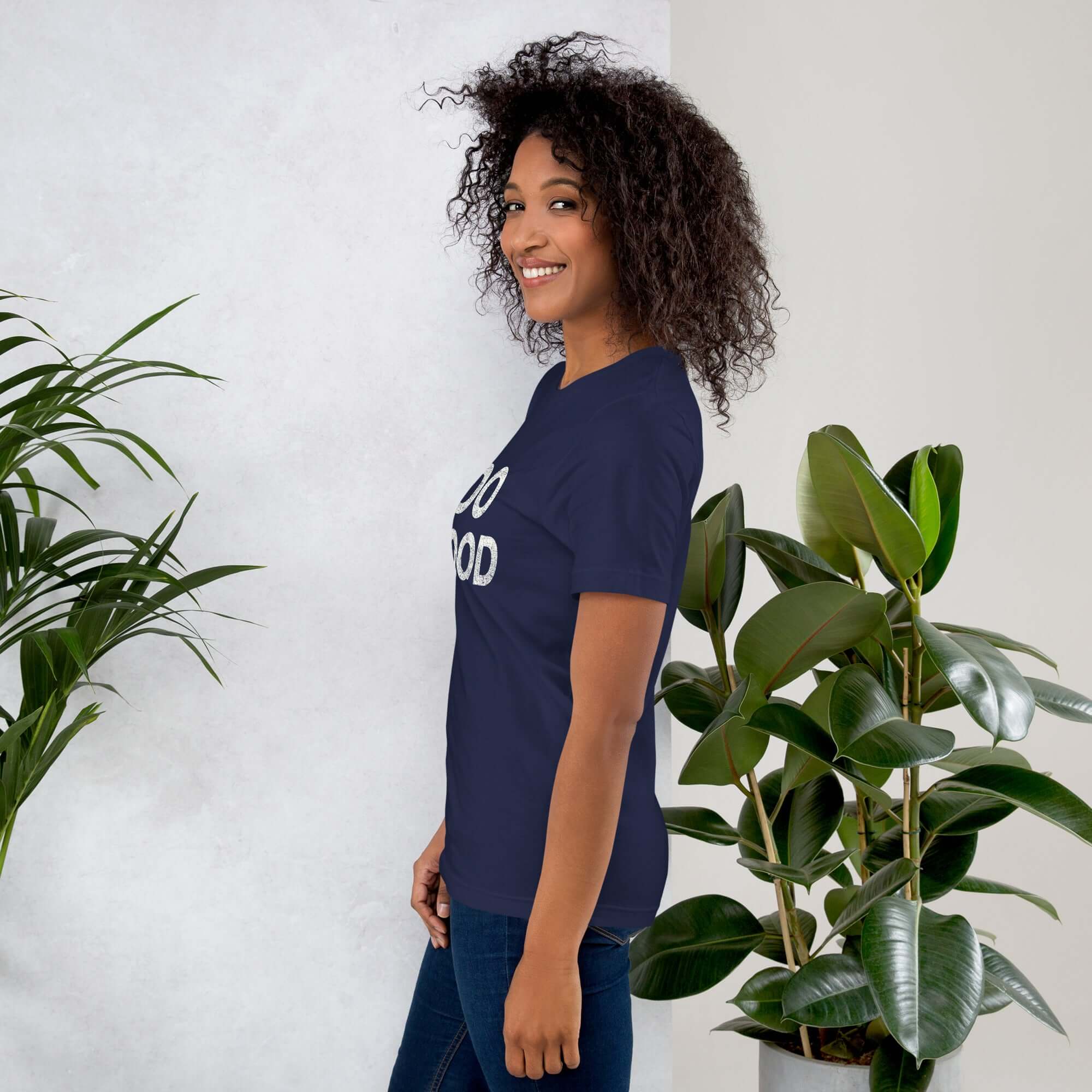 Side view of smiling woman wearing navy Milk Sandwich T-shirt with DO GOOD slogan, standing near indoor plants, minimalist inspirational tee.