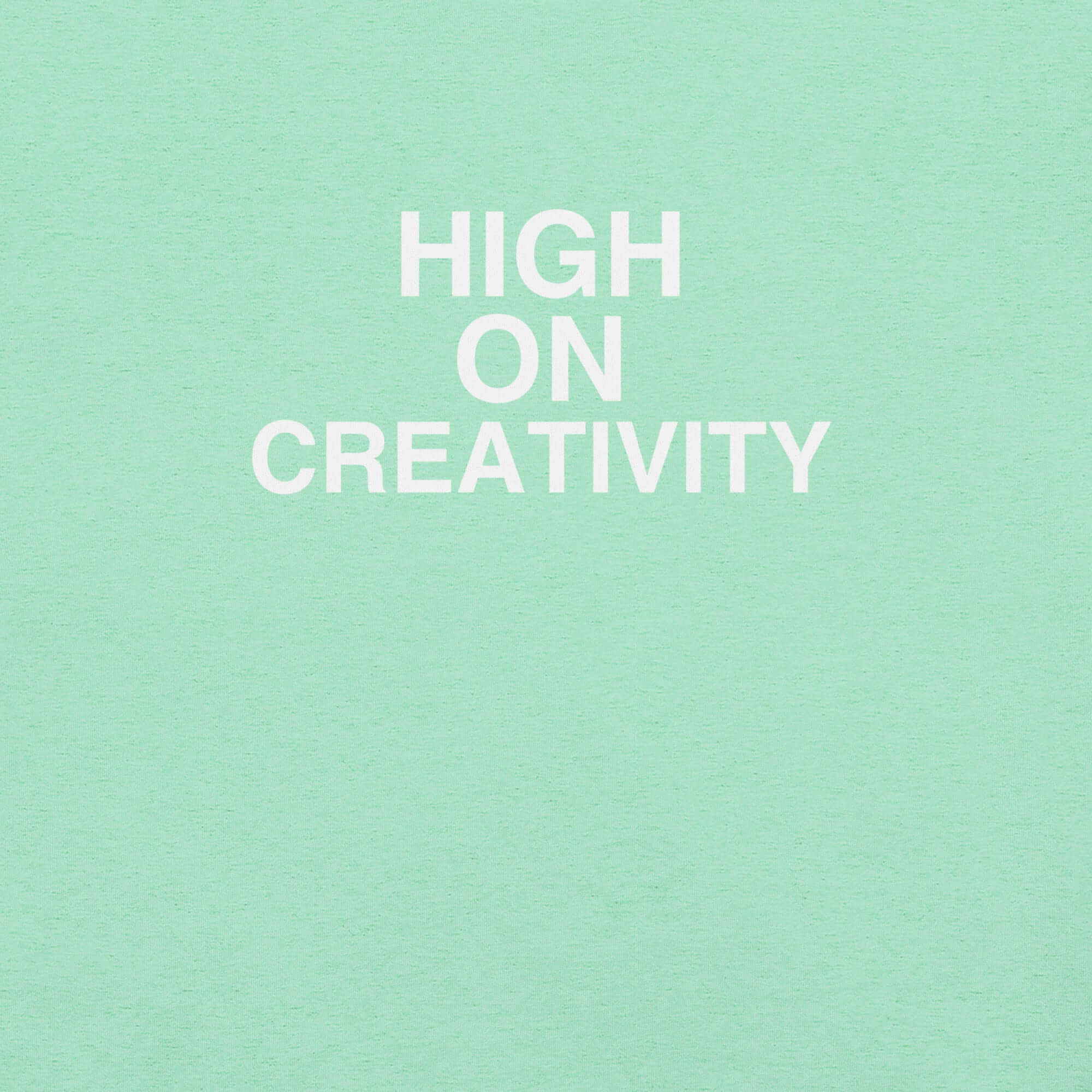 Close-up of mint t-shirt fabric with the phrase “HIGH ON CREATIVITY” printed in bold white uppercase letters in three lines.