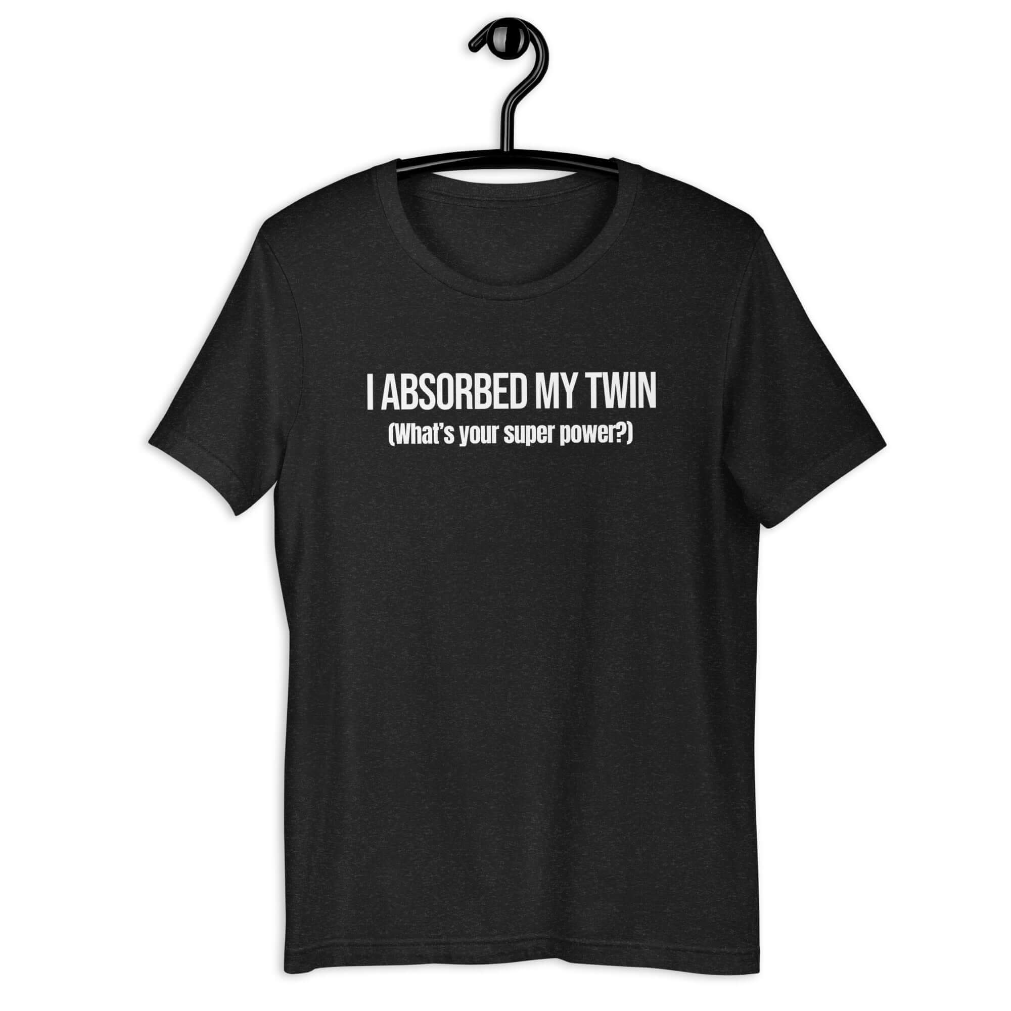 Black t-shirt hanging on a hanger with white text “I ABSORBED MY TWIN (What’s your super power?)” on the front.         
