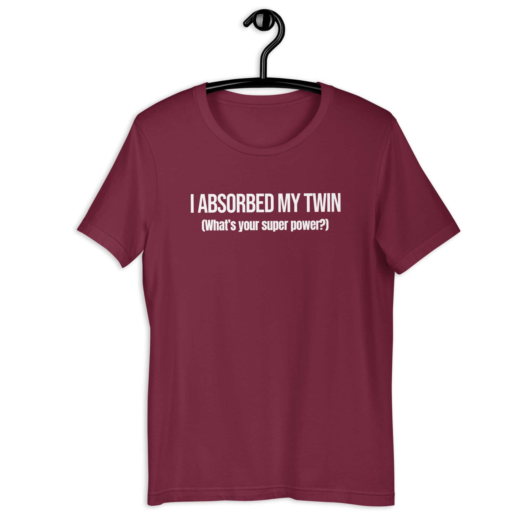 Maroon t-shirt hanging on a hanger with white text “I ABSORBED MY TWIN (What’s your super power?)” on the front.       