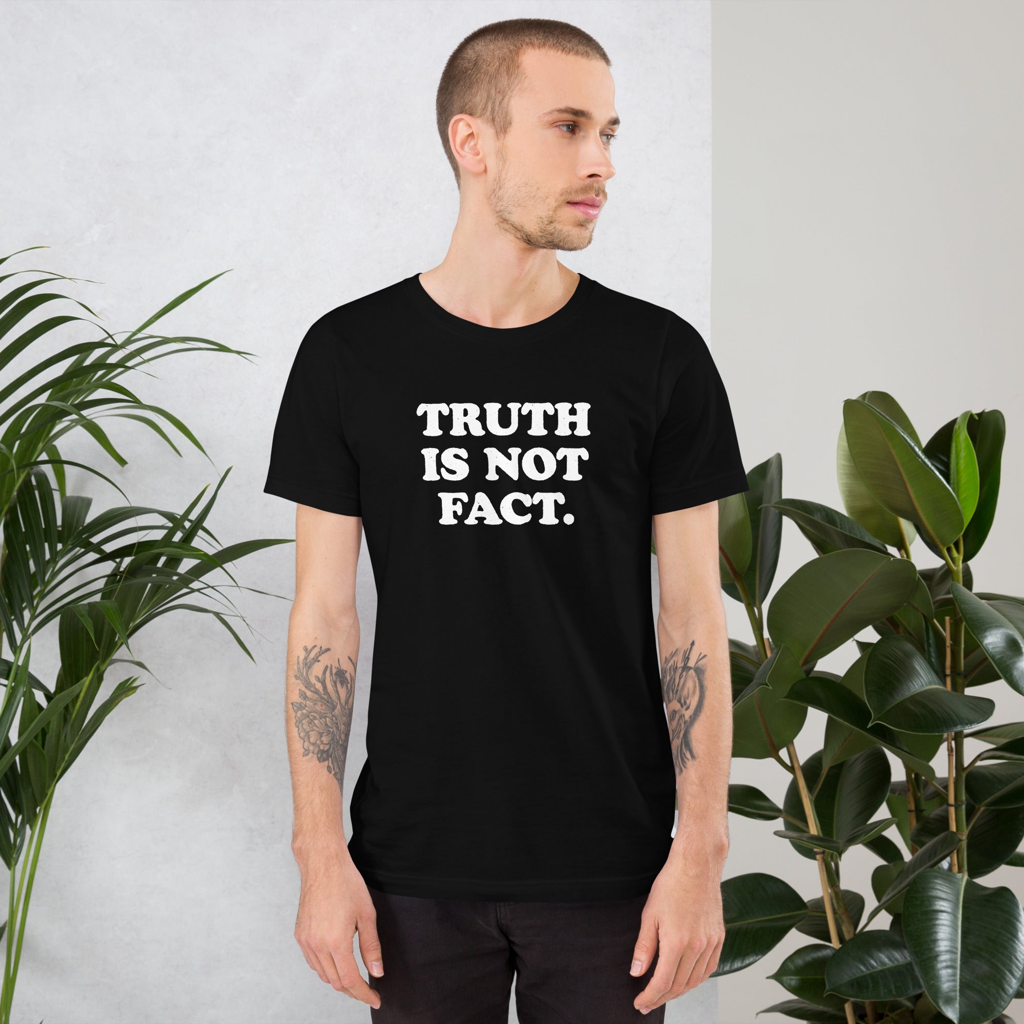 Unisex t-shirt featuring &#39;Truth is Not Fact&#39; text, shown with a model in a stylish, modern setting surrounded by greenery.