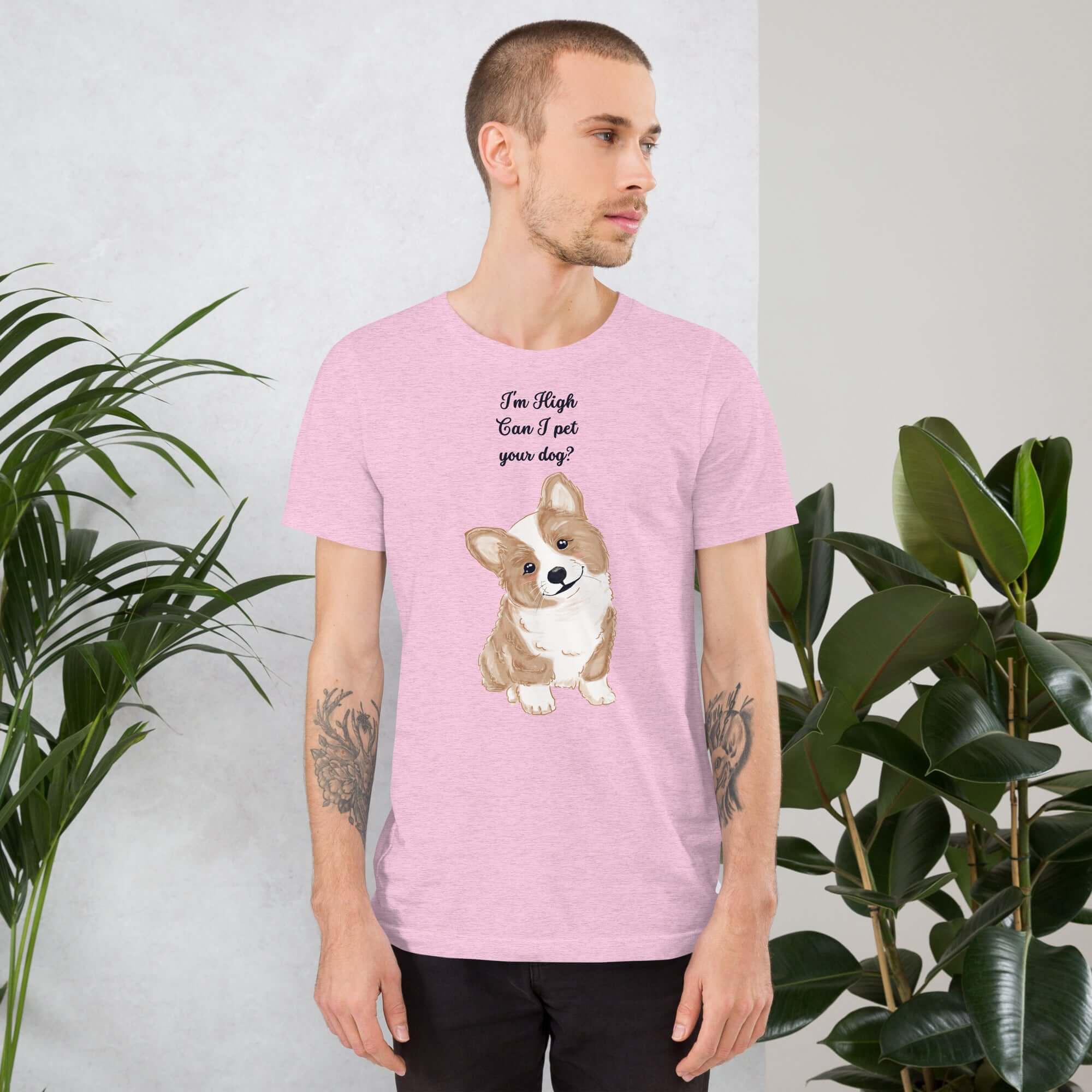 Man wearing a pink unisex t-shirt with a cute corgi design and the text &quot;I&#39;m High, Can I pet your dog?&quot; surrounded by plants.