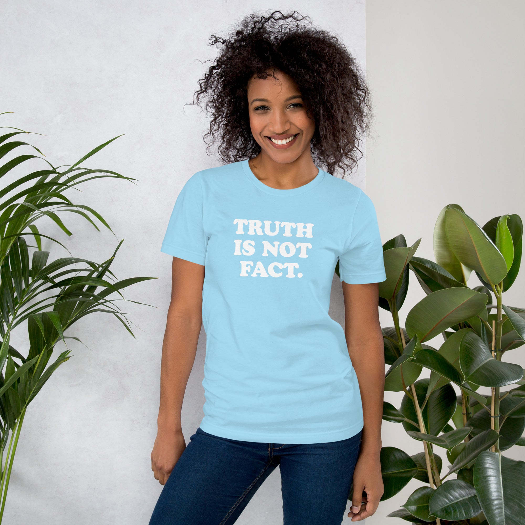 Unisex t-shirt in light blue with &quot;TRUTH IS NOT FACT.&quot; message, paired with indoor plants for a vibrant look.